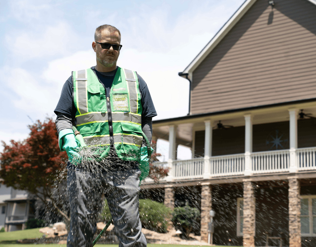 WeedPro technician in protective vest and gloves adjusting a spray wand on a homeowner’s lawn to ensure proper sprinkler performance.
