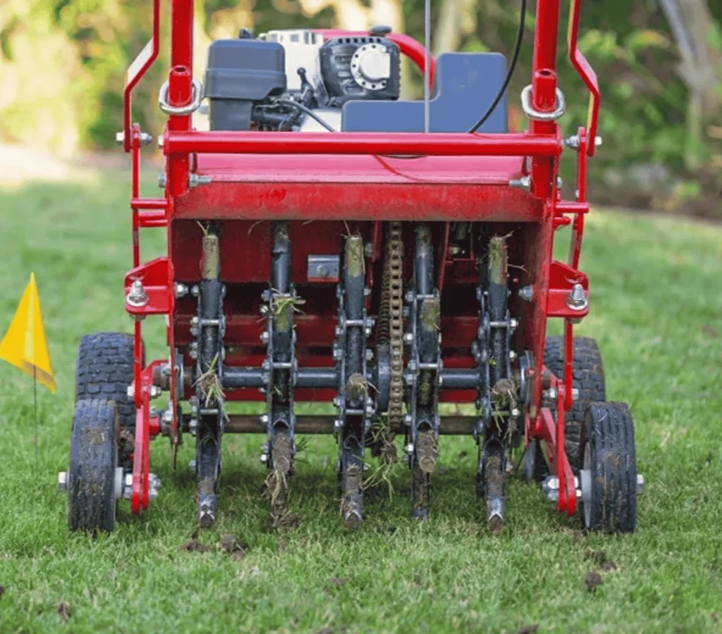 Rear view of a core-aerator machine puncturing lawn soil, removing small plugs for improved root growth.