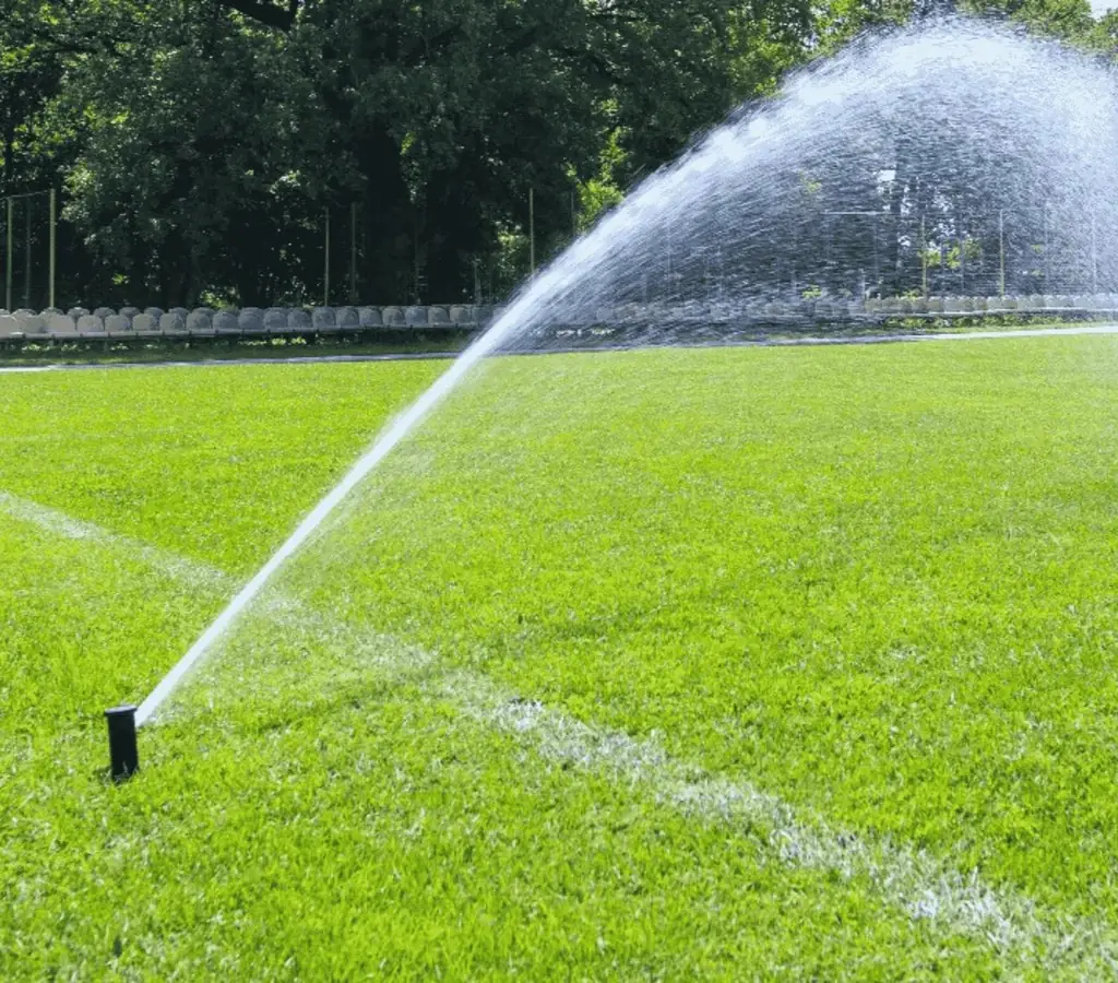 Fine mist of liquid aerator solution dispersing over a well-kept sports field to improve soil health.