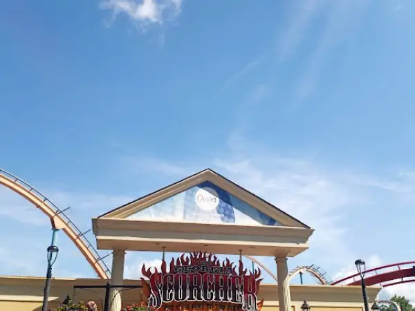Georgia Scorcher roller coaster entrance with blue sky and amusement park rides in the background.