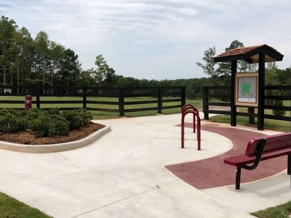 Lawn care service area in Ball Ground, GA, featuring a landscaped park entrance with seating, bike rack, and informational sign amidst green fields and trees.
