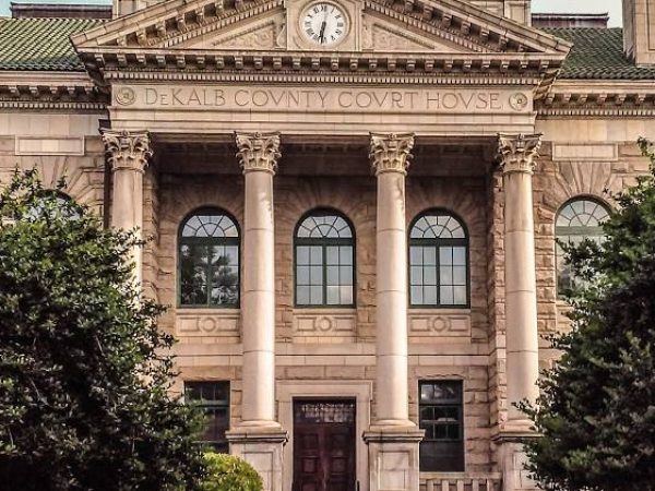 DeKalb County Courthouse facade with classical architecture, featuring columns and large windows, surrounded by greenery.