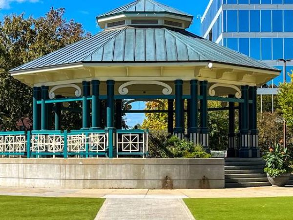 Gazebo in a landscaped park setting with green grass, surrounded by trees and modern buildings, representing community spaces in DeKalb County, GA.