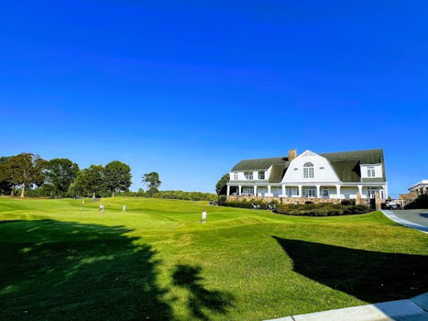 Lush green lawn with golfers practicing on a well-maintained golf course beside a white clubhouse under a clear blue sky in DeKalb County, GA.