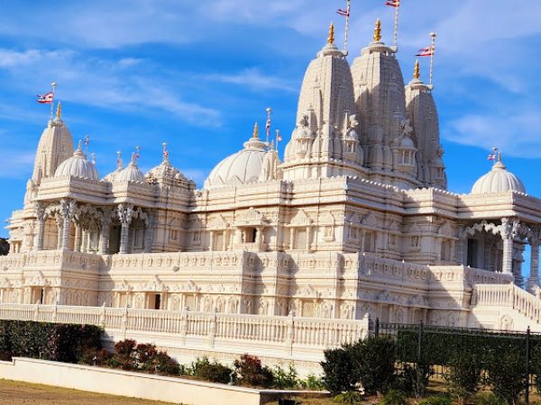 Hindu temple with intricate white stone architecture, domes, and flags against a blue sky, representing cultural heritage in Gwinnett County, GA.