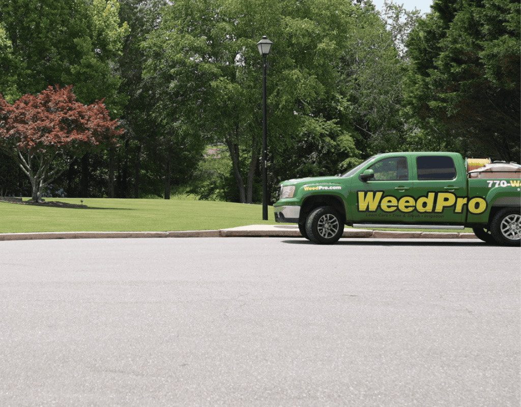 A WeedPro pickup and service truck parked on a curved road beside a freshly mowed lawn, ready for core aeration services.