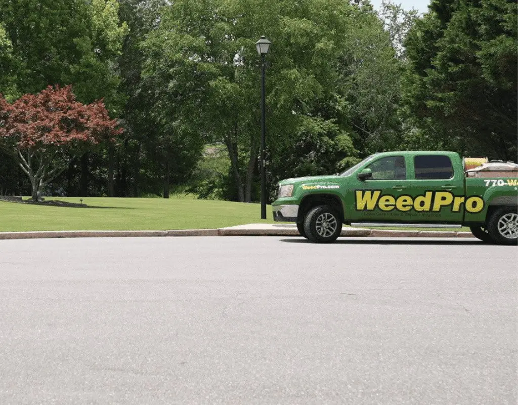 A WeedPro pickup and service truck parked on a curved road beside a freshly mowed lawn, ready for core aeration services.