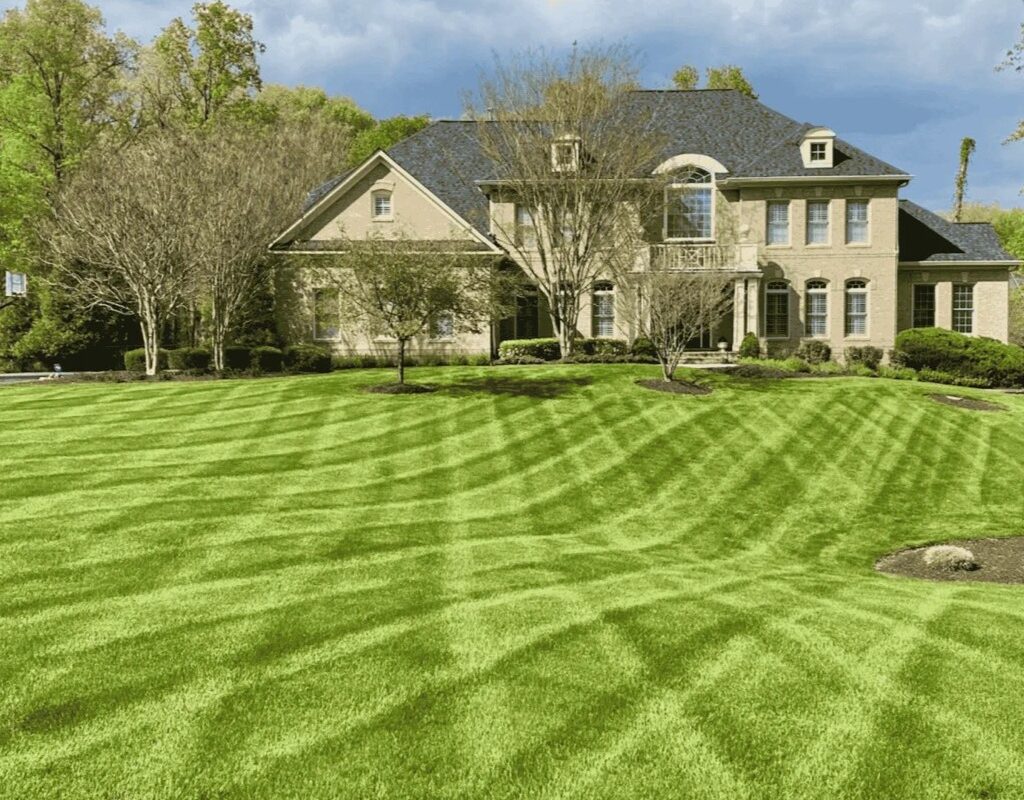 Lush, well-manicured lawn with striped pattern in front of a large, elegant home, showcasing the benefits of professional lawn care and pest control services in Milton, GA.