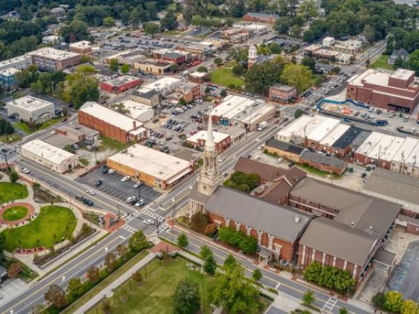 Aerial view of downtown Lawrenceville, GA, showcasing vibrant commercial buildings, green spaces, and the historic church steeple, reflecting the community's charm and appeal for residential and commercial lawn care services.