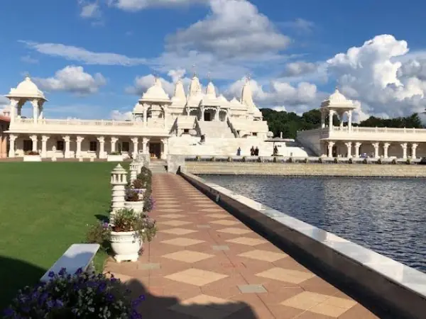 Scenic view of a beautifully landscaped pathway leading to a grand white temple by a serene water body, surrounded by lush greenery and decorative flower pots, reflecting the commitment to aesthetic appeal in Gwinnett County, GA.