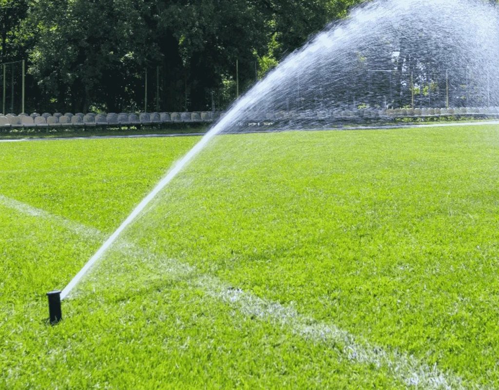 Fine mist of liquid aerator solution dispersing over a well-kept sports field to improve soil health.