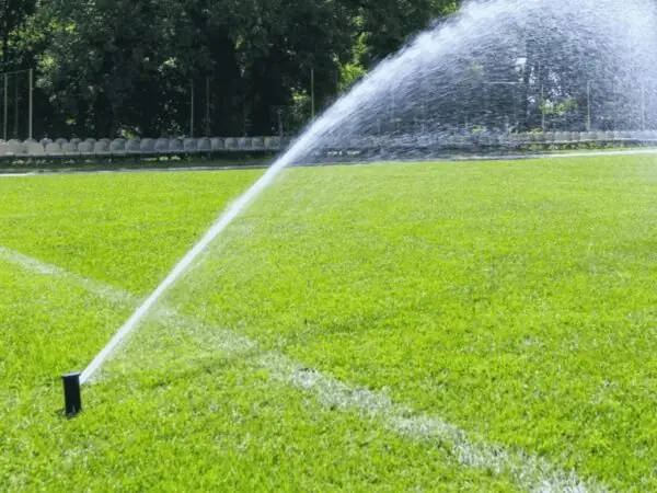 Fine mist of liquid aerator solution dispersing over a well-kept sports field to improve soil health.