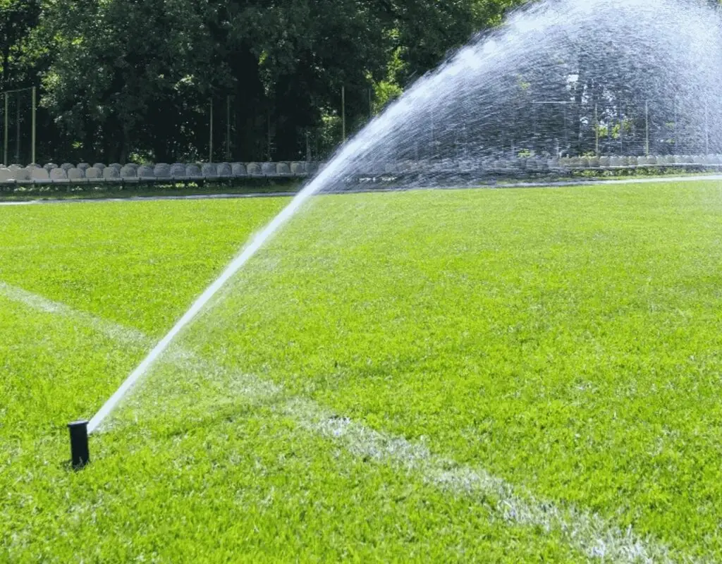 Fine mist of liquid aerator solution dispersing over a well-kept sports field to improve soil health.