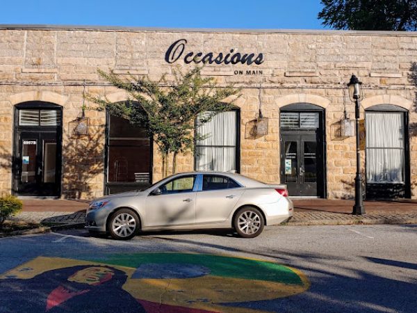Occasions on Main storefront in Lithonia, GA, featuring a silver sedan parked in front and colorful mural on the ground.