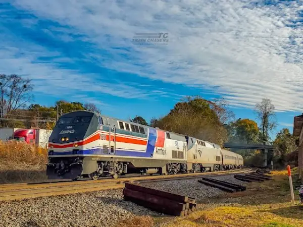 Amtrak train traveling along tracks in a scenic landscape, featuring a clear blue sky and autumn foliage, highlighting transportation in Cobb County, GA.