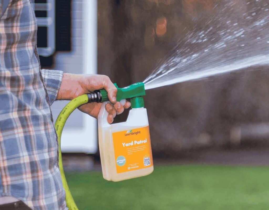 Person using a spray bottle labeled "Yard Patrol" connected to a hose for lawn care, demonstrating effective lawn maintenance practices relevant to Weed Pro Lawn Care's fertilization services in Duluth, GA.
