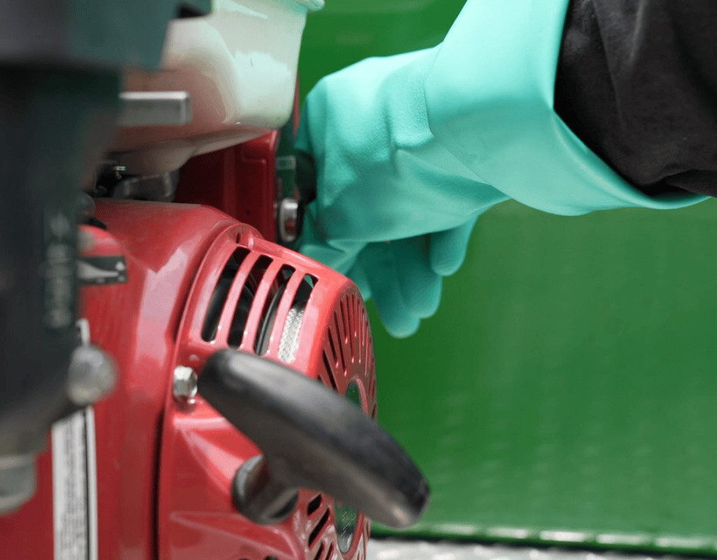 Close-up of a technician’s green chemical-resistant glove adjusting controls on a red pump sprayer, prepping a plant growth regulator application.