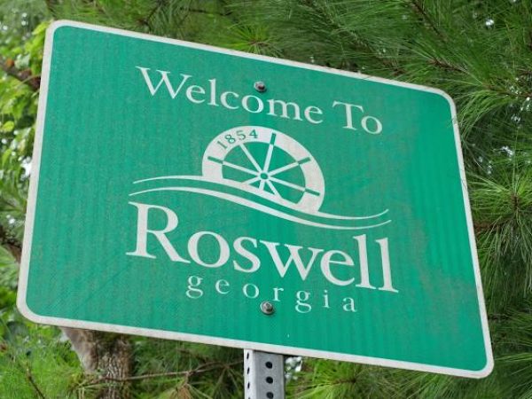 Welcome to Roswell, Georgia sign featuring a green background, decorative wheel emblem, and established date 1854, surrounded by greenery.