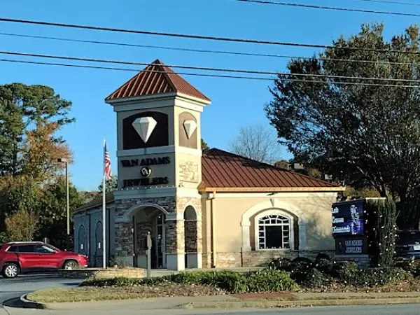 Jewelry store exterior featuring the Van Adams Jewelers building with a diamond-shaped sign, surrounded by landscaping and a red car parked nearby, located in Snellville, GA.