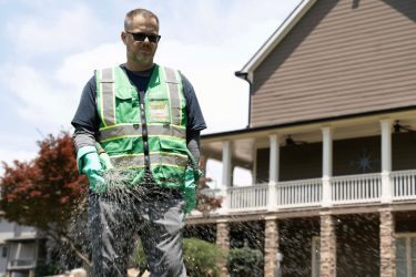 WeedPro technician in protective vest and gloves adjusting a spray wand on a homeowner’s lawn to ensure proper sprinkler performance.