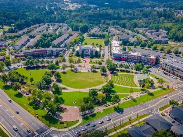 Aerial view of a vibrant park in Suwanee, GA, surrounded by residential buildings and commercial establishments, showcasing green lawns, walking paths, and recreational areas, emphasizing community spaces in Gwinnett County.